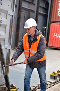 Man wearing safety vest and helmet working with metal rod on a container in port, worker working on