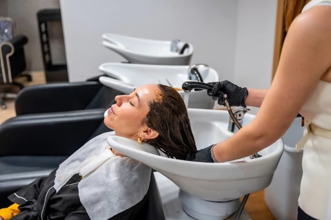 Professional stylist washing a woman's hair in a salon sink, applying post color treatment for