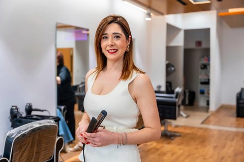 Professional hairdresser in a salon holding a flat iron, smiling confidently while preparing to