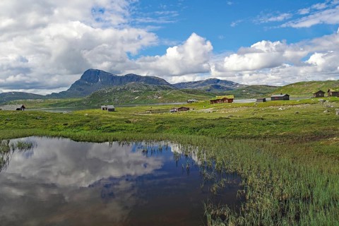 Lakeside mountain hut with clear reflections of mountains and clouds in water, Bygdin,