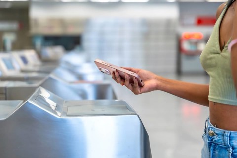 Woman using contactless mobile payment at a subway turnstile, entering the station during her daily