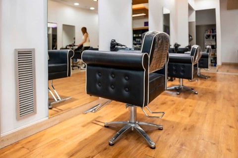 Hair salon interior featuring empty black leather styling chairs with white piping, reflective wall