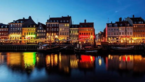 Bunte, beleuchtete Fassaden spiegeln sich nachts im Wasser eines belebten Kanals, Kopenhagen,