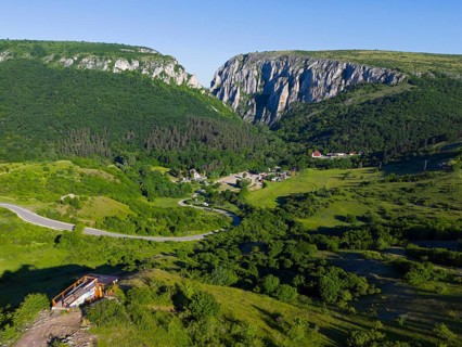 A picturesque landscape with green hills, a small village and impressive cliffs in the background,