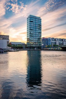 A high-rise building is reflected in calm water at sunset in an urban setting, Docklands Dublin,