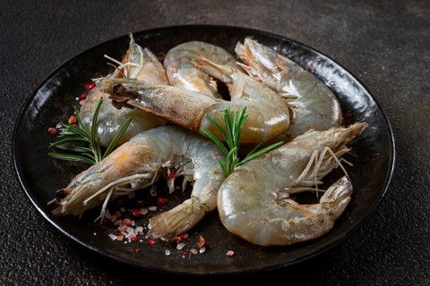 Fresh raw white-footed shrimp, tiger prawns vannamei, on a black plate, with spices and herbs