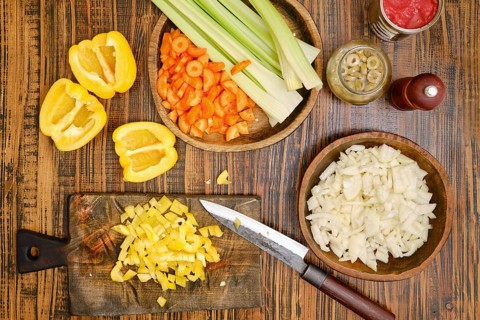 Vegetables are prepared on a wooden table. Yellow pepper slices are next to chopped onions and
