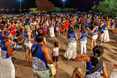 A large group of people joyfully dances at night to music with drums, joy and dance at a festival