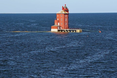 A red lighthouse stands isolated in the blue sea in calm weather, Kjeungskjær fyr, Trøndelag.