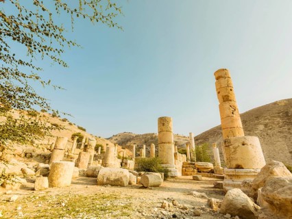 Weathered stone columns standing among fallen blocks archaeological ruins hillside background clear