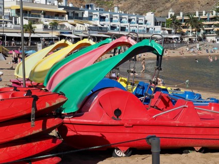 Colourful paddleboats on sunny beach with bathers and sea in the background, Puerto de Mogan, Gran