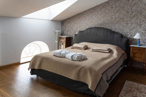 A cozy attic bedroom features a dark upholstered bed with a beige bedspread and matching pillows.