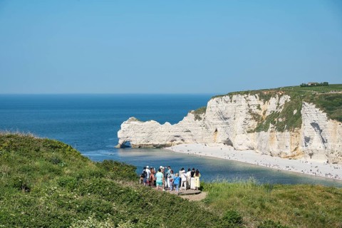 Tourists stand at a viewpoint on the Falaise d'Aval and look at the pebble beach of the seaside