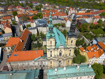 Aerial view of a baroque church with towers, surrounded by urban structures and green surroundings,