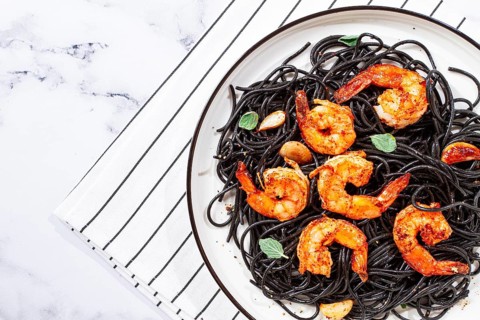 Black spaghetti with shrimp, on a white plate with a fork, on a striped napkin, marble background,