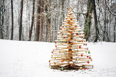 Beautiful handmade wooden Christmas tree decorated with festive balls in a snowy forest in winter