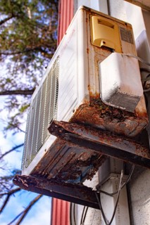 An old and rusty air conditioner hanging on the hotel building, in the sunny outdoor, seaside