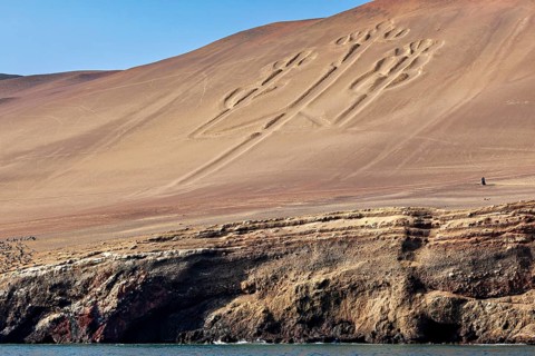 A geoglyph of the candelabra rises above the calm ocean water, candelabra of Paracas in Peru
