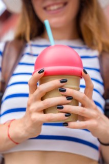 Young woman holding a stylized ice cream cone cup with a pink dome lid and blue straw, smiling