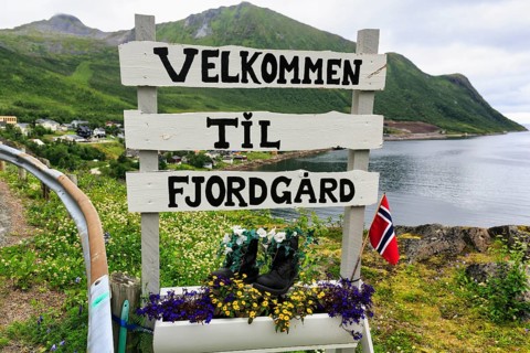 Town entrance sign of the small fishing village of Fjordgard, inscription welcome, coastline on the