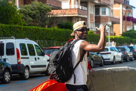 Young black man smiling and signaling shaka with beach equipment, enjoying summer lifestyle and