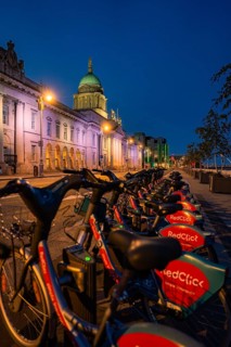 Row of rented bikes in front of illuminated historic and modern buildings, Dublin, Ireland