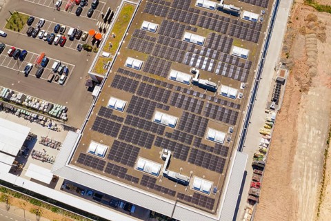Building with solar panels on the roof, next to a parking lot with cars. Industrial area, PV plant
