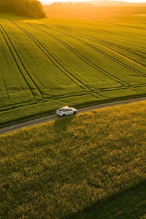 A car drives on a narrow road between wide fields in the evening light, Tesla Model Y, Gechingen,