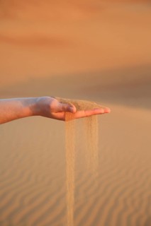 Sand flows gently from an outstretched hand in a quiet dune desert, a woman's hand lets red desert