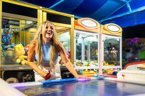 Young woman playing air hockey at a vibrant night amusement park, smiling and celebrating a moment