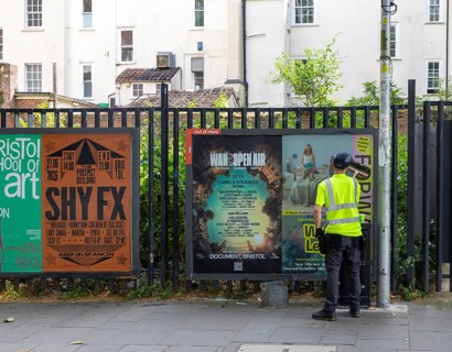 Man brushing vent poster onto advertising board space in city centre of Bristol, England, UK