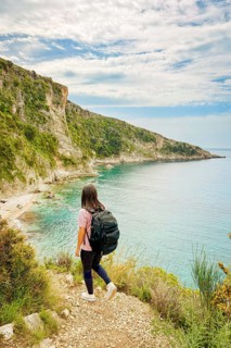 Aerial view woman hiking on viewpoint isolated go down to Filikuri beach in spring. Clear turquoise