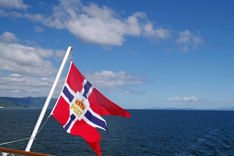 A Norwegian flag blowing in the wind over a clear blue sea and sky, mail ships, Havilla, Trondheim,