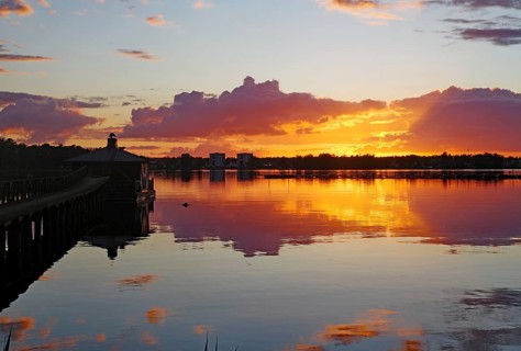 The sky glows orange and purple at sunset with clouds and reflections on the still water surface,