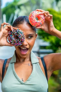 Young woman playfully covering her eyes with two vibrant sprinkle covered donuts while expressing