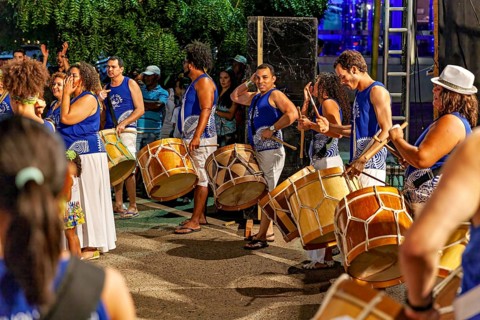 Group of drummers in blue shirts play at an event in the evening, a band plays and dances at a