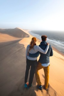 Young couple standing on a dune in front of an impressive desert landscape, sand dunes and sea in