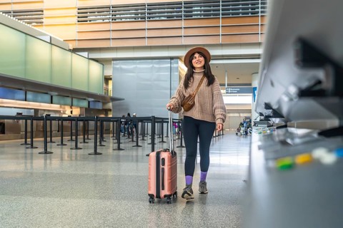 Woman smiling, walking confidently through a modern airport terminal pulling her suitcase,