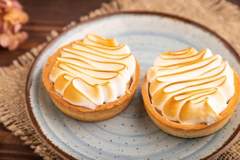 French lemon tart with meringue on brown wooden background, cup of coffee, linen textile, side