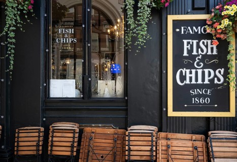 Wooden folding chairs lean against the exterior of a black-painted restaurant, traditional fish &