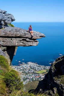 Young woman sitting on an imposing rock pin on a cliff, view of sea and coast, Kasteelspoort