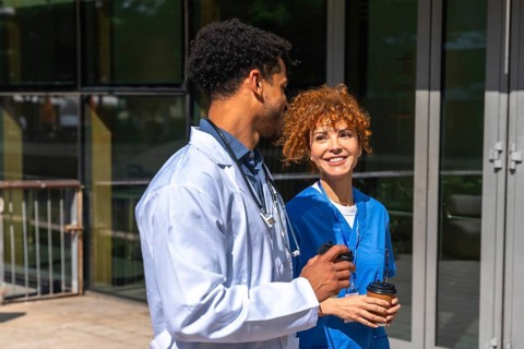 Medical team members, a male doctor wearing a white coat and a female nurse in blue scrubs, smiling
