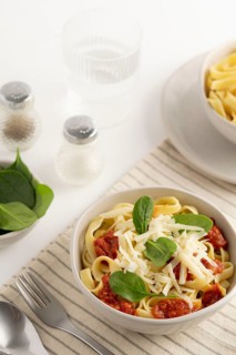 A bowl of spaghetti topped with tomato sauce, grated cheese, and fresh spinach leaves. Beside it, a