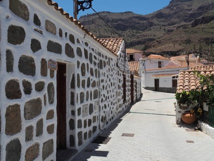 Alley in Fataga with brick buildings and mountainous background in sunny weather, Barranco de