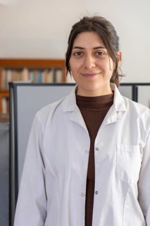 Headshot portrait of a young brunette female scientist in a white lab coat smiling gently at the