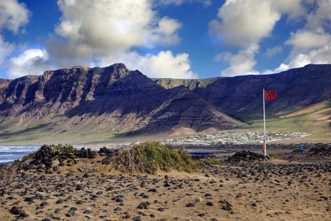 Coastal landscape with Famara cliffs (Risco de Famara) and a red flag in the wind, Caleta de Famara