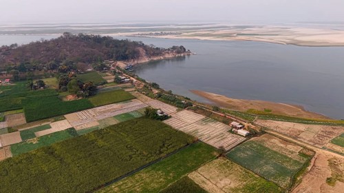 Aerial view of cultivated farmland along the riverbank, with patchwork fields stretching toward a