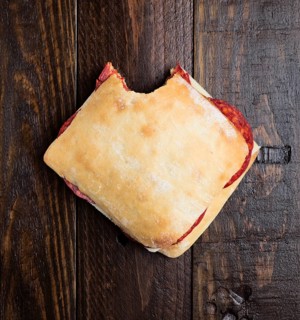 Top view of a homemade chorizo sandwich with a bite taken out, placed on a rustic wooden surface