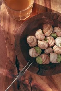 Snails cooked with herb oil on a wooden plate, served with white wine, natural light, no people
