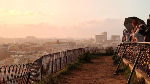 People with umbrellas and love locks at a viewpoint in Lisbon enjoying a romantic evening mood,